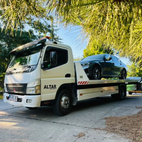 Koyu renk otomobil ağaçlı sokakta çekici platformunda